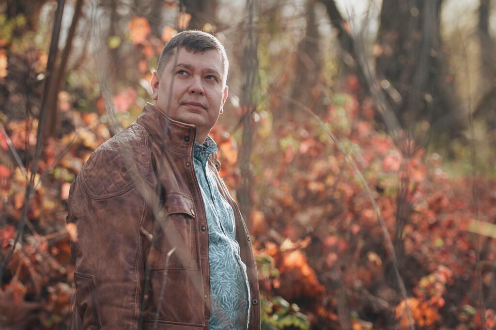 Mężczyzna, Marcin Wargocki w skórzanej kurtce w lesie.